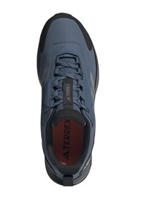 Zapatilla atlética de tejido azul con acentos negros, parte superior texturizada y cierre con cordones. Presenta una plantilla acolchada y suela de goma.