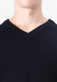 Pull marin en V de couleur bleu marine, fabriqué à partir d'un tissu tricoté doux, avec un col côtelé, présentant une texture lisse et un design minimaliste.