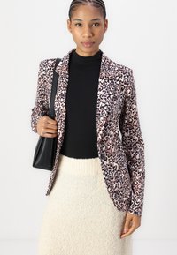 Leopard-print blazer with a tailored fit, soft fabric, dark lapels, and two front pockets; paired with a textured light skirt and black top.