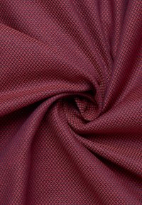 Tessuto texturizzato di un rosso intenso con un motivo geometrico a rombi. Morbido, dalla superficie liscia e con una leggera lucentezza. Ideale per abbigliamento o tappezzeria.