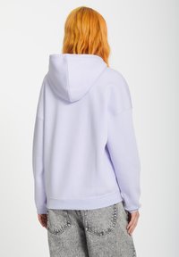 Lila hoodie met een relaxte pasvorm en capuchon, met afgeknipte schouders en geribde manchetten, gecombineerd met grijze geblokte broeken.