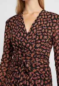 Svart omslagsklänning med långa ärmar, prydd med ett paisleymönster i nyanser av orange och lila. Knytning i midjan med texturerat tyg.