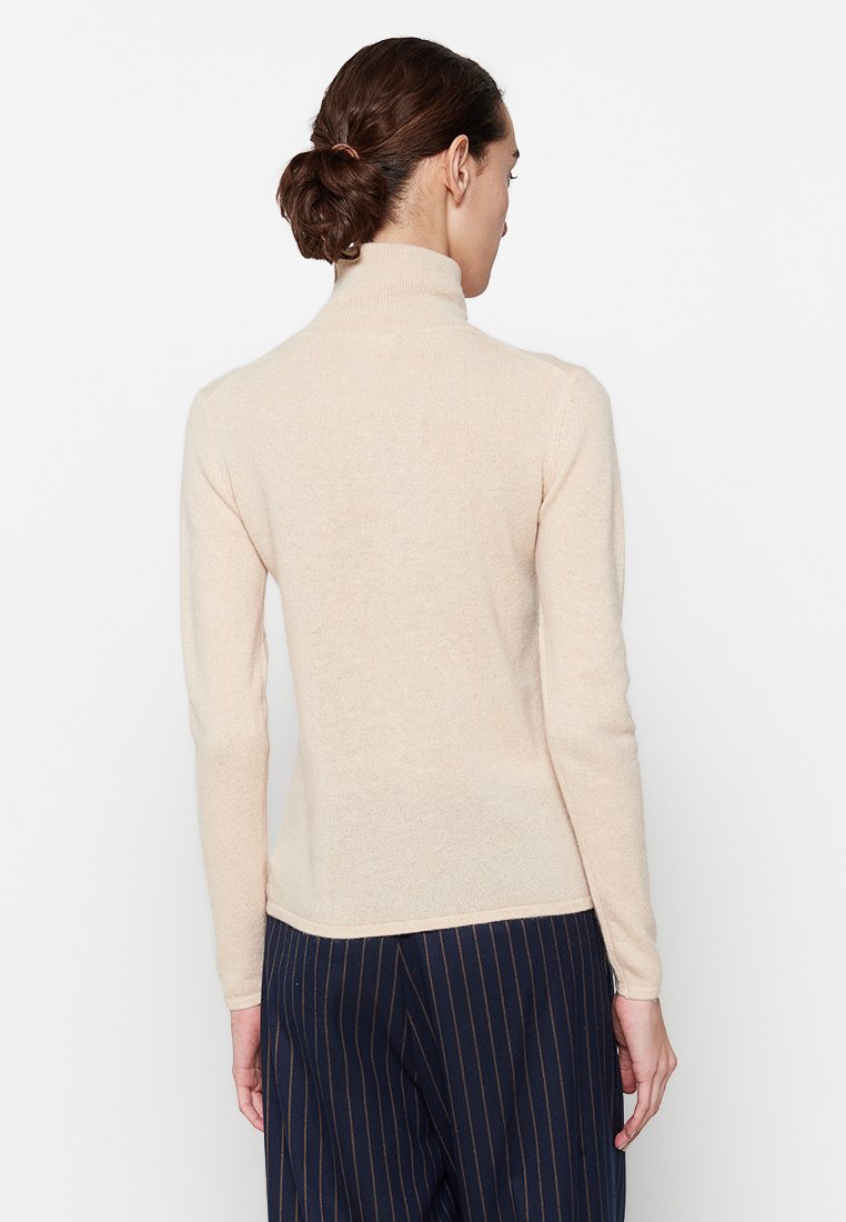 Jasno beżowy sweter z golfem, wykonany z miękkiego, teksturowanego materiału. Dopasowany krój z długimi rękawami i czystym wykończeniem, w zestawie ze spodniami w prążki.