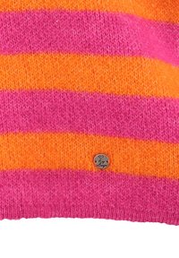 Tissu en maille avec des rayures horizontales orange et rose, avec une petite étiquette métallique ronde gravée d'un cœur et d'un texte en écriture cursive.
