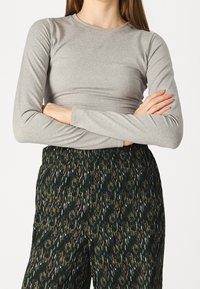 Light gray long-sleeve top with a round neckline, paired with dark green textured pants featuring a subtle animal print pattern.