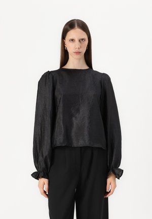 Svart teksturert bluse med lange, puffete ermer og rund hals. Materialet har en subtil glans. Bært med løse svarte bukser.