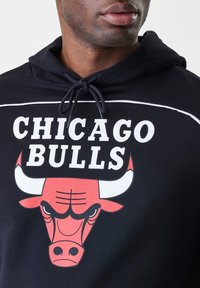 Crna kapuljača od pamuka s vezicom. Sadrži tekst "CHICAGO BULLS" i grafiku crvene bikove na prednjoj strani.
