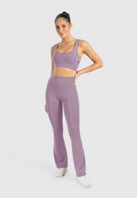 Lichtpaarse sportbeha en high-waisted legging, gemaakt van gladde, rekbare stof met een naadloos ontwerp en minimale merkaccenten.