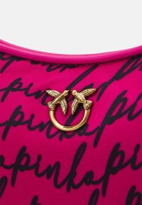 Tissu rose vif avec texte en script noir. Ornements décoratifs en métal doré avec deux oiseaux encerclant un anneau au centre. Texture lisse.