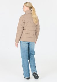 Beige pufferjakke med høj krave, quiltet design og lange ærmer, parret med lyseblå brede jeans og sorte sneakers.