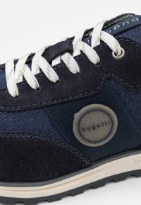 Temno modri kopalci z usnjem in denima, belimi vezalkami in okroglim sivim logom na strani. Teksturirana gumijasta podplat.
