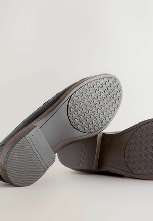 Fekete cipők, textúrázott gumitalppal, sima felülettel és barna díszítéssel a széleken. Részletes futómintázat jellemzi.