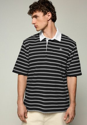Black and white striped polo shirt with a white collar, short sleeves, and a small embroidered logo on the chest. Cotton material, relaxed fit.