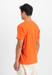 Oranges Baumwoll-T-Shirt mit kurzen Ärmeln, Rundhalsausschnitt und lässiger Passform, das eine glatte Textur aufweist und keine sichtbaren Logos oder Muster hat.