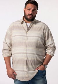 Camisa de botón de color beige claro con rayas horizontales en colores suaves. Mangas largas remangadas, combinada con jeans de mezclilla desgastados.
