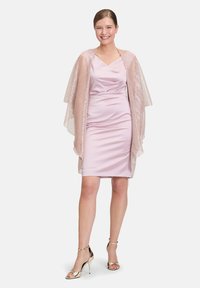 Lichtroze satijnen jurk met een gedrapeerde halslijn, gecombineerd met een sheer, gemuste omslagdoek. Het model draagt metallic gouden hakken.