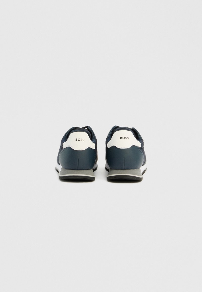 Baskets de sport bleu marine avec un talon blanc et gris. Présentent un matériau texturé et un logo "BOSS" bien en vue sur le talon et la languette.