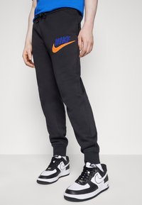 Svarta Nike sweatpants med orange och blå logotyp, elastisk midja och smalnade muddar, ihopparat med svarta och vita Nike-skor.