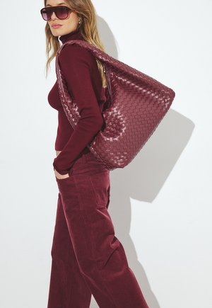 Vīnsarkanā pinuma ādas soma ar vaļēju formu, saskaņota ar atbilstošu augstu apkakli un kordurojas biksēm. Liela, spīdīga virsma.