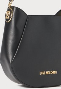 Black leather shoulder bag with rounded shape. Features a gold-tone logo and hardware accent. Smooth texture with minimalistic design elements.