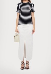 Pruhované námořnické modré a bílé bavlněné tričko, bílé maxi sukni s předním rozparkem, béžovou kabelku, černé sandály na podpatku.