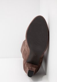 Botín de ante marrón con puntera puntiaguda, que cuenta con una suela de goma negra lisa y detalles de costura sutiles. Talla marcada como 37 en la suela.