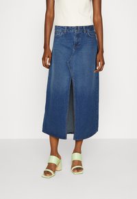 Jupe maxi en denim dans un lavage foncé avec une fente avant et des coutures traditionnelles. Associée à des sandales à talons blocs vert menthe.