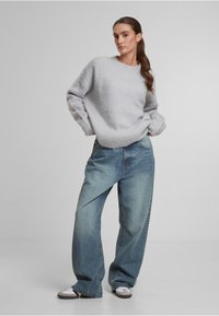Grauer, strukturierter Pullover mit Rundhalsausschnitt, kombiniert mit lockeren, hellblauen Jeans aus Denim mit hoher Taille und weitem Bein.