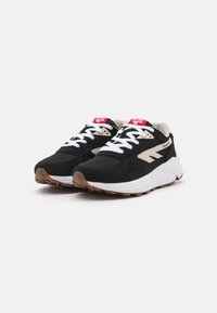 Black and beige sneakers with a mesh and suede upper, white laces, and a brown rubber sole. Features a prominent brand logo on the side.