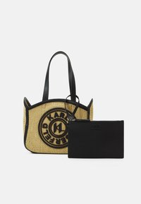Sac cabas beige tissé avec bordure noire et logo, accompagné d'une pochette noire zippée, tous deux avec des poignées et des détails en cuir.