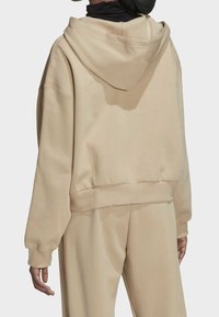 Béžová mikina s kapucí, dlouhými rukávy, žebrovanými lemy na rukávech a lemu spodní části. Měkká látka, minimalistický design bez viditelných vzorů.