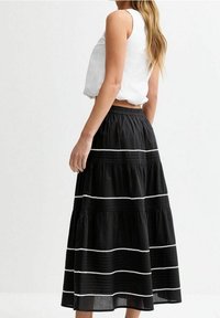 Mustalainen maksimekko, jossa on kerroksia ja valkoisia viivakorostuksia. Sen vyötärössä on joustava vyötärönauha ja se on valmistettu kevyestä, virtaavasta kankaasta.