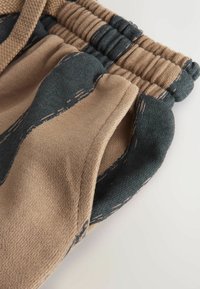 Shorts de jogging à motifs marron et vert avec un tissu texturé, une taille élastique et des poches latérales.