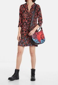 Černá květinová blůza s červenými akcenty, vzorovaná minisukně, černé šněrovací boty a barevná květinová kabelka přes rameno.