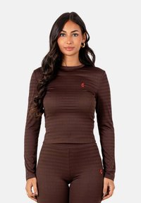Bruine geribde lange mouw top met een ronde hals en een klein rood logo op de borst. Gecombineerd met bijpassende bruine leggings.