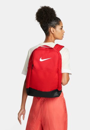Rød Nike rygsæk med stort hvidt logo, har en sort base, justerbare stropper og tekstureret stof med en frontlomme med lynlås.