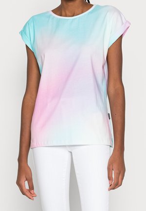 Person iført en pastel tie-dye t-shirt med korte ærmer i blå, pink og hvid, kombineret med hvide bukser, vist fra hals til hofter.