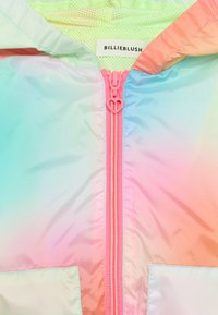 Ελαφρύ, ιριδίζον μπουφάν με διαβαθμισμένο μοτίβο σε παστέλ χρώματα. Διαθέτει ροζ φερμουάρ σε σχήμα καρδιάς και επένδυση από δίχτυ στο εσωτερικό.