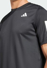 Camiseta deportiva negra hecha de un tejido suave y ligero. Presenta un escote redondo y un logo triangular blanco en el hombro izquierdo.