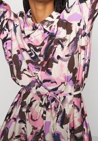 Musteriertes Hemdkleid in Pink, Lila und Braun. Verfügt über einen Kragen, eine durchgehende Knopfleiste, eine Kordelzug-Waist und einen fließenden Stoff.