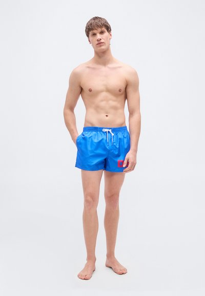 Μπλε μαγιό σορ τς από λείο υλικό, με ελαστική μέση και κορδόνι, καθώς και κόκκινη λεπτομέρεια λογότυπου στην αριστερή πλευρά.