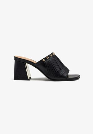 Mules noirs avec des franges et des clous dorés. Bout carré et un talon bloc moyen avec un accent métallisé à l'arrière. Fini en cuir lisse.
