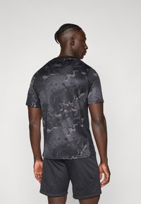 T-shirt de sport noir avec un motif texturé sombre composé de formes géométriques et organiques. Manches courtes et col rond.