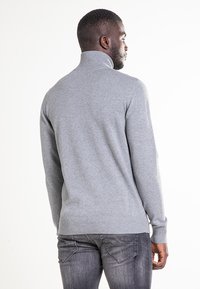 Szary sweter z wysokim kołnierzem wykonany z miękkiego materiału, z długimi rękawami oraz ściągaczami na mankietach i dole. Gładka faktura i dopasowany fason.