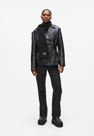 Black leather biker jacket with belt, ribbed texture, and embroidered accents. Paired with a black scarf and fitted black pants, and platform boots.