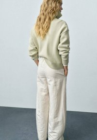 Creamy green oversized sweater with a high collar, paired with loose, white linen pants. Both garments feature soft textures.