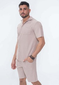 Chemise légère marron clair à manches courtes et short assorti en tissu texturé avec un motif rayé vertical. Comprend une poche poitrine.