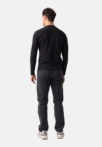 Czarna, długosleeve koszula o dopasowanym kroju, w połączeniu z ciemnoszarymi dżinsami. Model nosi jasne sneakersy. Gładkie tło.