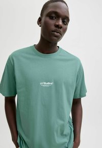 Heleroheline lühikeste varrukatega puuvillane t-särk. Ees valge logotekstiga. Pehme tekstuur ja lõdvestunud istuvus.