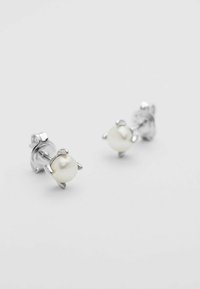 Gli orecchini a bottone in argento presentano perle bianche rotonde fissate con impostazioni a quattro artigli. Texture liscia con finitura lucida. Design semplice.